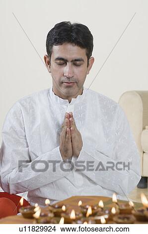 Close-up of a mid adult man praying with oil lamps in front of him View Large Photo Image Picture - Close-up of a mid adult man praying with oil lamps in front of him. Fotosearch