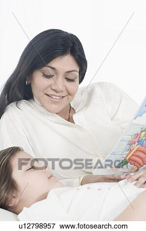 Close-up of a mid adult woman looking at her daughter reading a book View Large Photo Image Stock Photo - Close-up of a mid adult woman looking at her daughter reading a book. Fotosearch