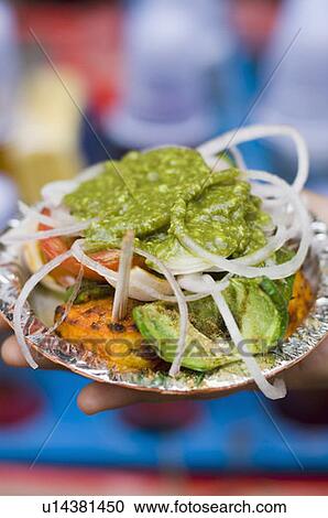 Stock Image - Close-up of a person's hand holding Paneer Tikka in a paper plate. Fotosearch