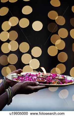 Stock Image - Close-up of a woman's hand holding oil lamps and Rose petals in a plate. Fotosearch