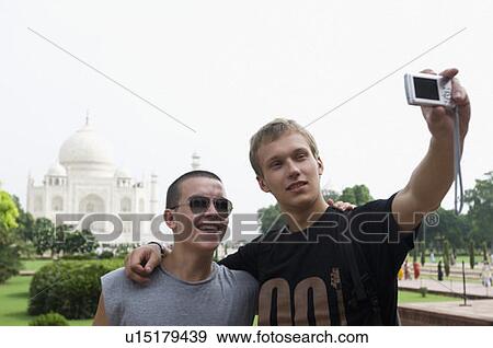 Close-up of a young man standing with his friend and taking a picture of themselves, Taj Mahal, Agra, Uttar Pradesh, India View Large Photo Image Stock Photo - Close-up of a young man standing with his friend and taking a picture of themselves, Taj Mahal, Agra, Uttar Pradesh, India. Fotosearch