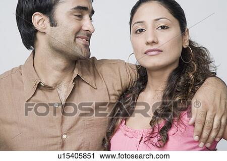 Stock Image - Close-up of a young man with his arm around a young woman. Fotosearch