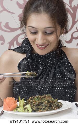 Stock Image - Close-up of a young woman eating food with chopsticks and smiling. Fotosearch