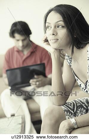 Stock Photography - Close-up of a young woman thinking with a young man using a laptop beside her. Fotosearch