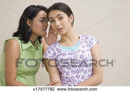 Stock Image - Close-up of a young woman whispering into another young woman's ear. Fotosearch