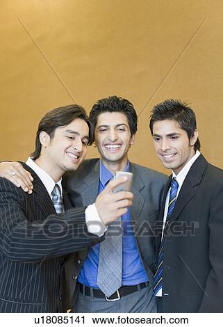 Stock Image - Close-up of three businessmen looking at a mobile phone and smiling. Fotosearch