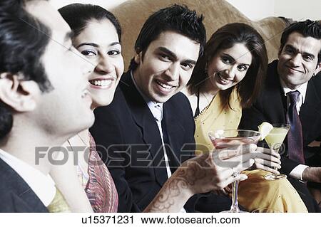 Stock Image - Close-up of three young men and two young women holding martini glasses. Fotosearch