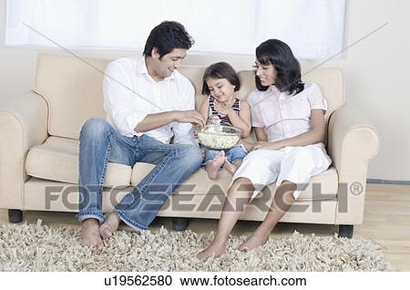 Stock Image - Family sitting on a couch and eating popcorn. Fotosearch
