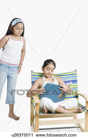 Girl holding a magazine with her sister standing behind her View Large Photo Image Stock Image - Girl holding a magazine with her sister standing behind her. Fotosearch