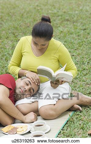 Stock Image - High angle view of a mid adult woman touching a mid adult man's forehead lying on her lap . Fotosearch