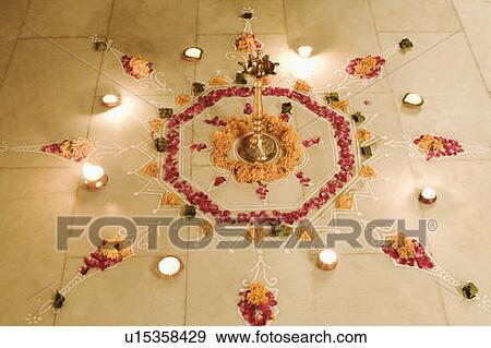 Stock Photo - High angle view of a Rangoli decorated with flowers and oil lamps on the floor. Fotosearch