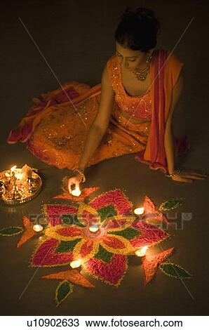 Stock Image - High angle view of a young woman decorating rangoli with oil lamps. Fotosearch