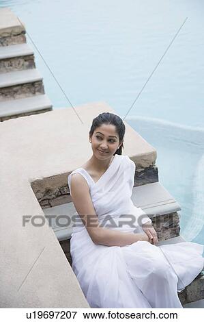 Stock Photo - High angle view of a young woman sitting at the poolside and smiling. Fotosearch