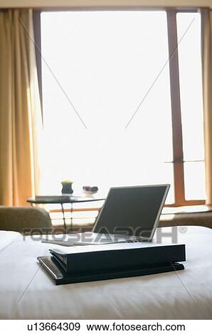 Stock Photo - Laptop with files on the bed in a hotel room. Fotosearch