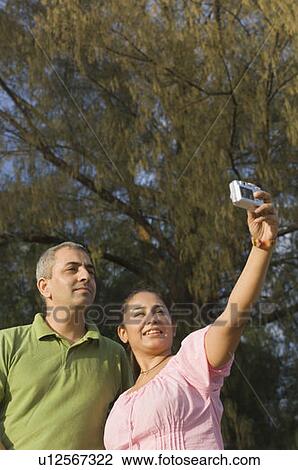 Stock Image - Low angle view of a mid adult couple taking a photograph of themselves. Fotosearch