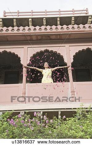 Low angle view of a young woman spreading flowers from the balcony of a fort, Neemrana Fort Palace, Neemrana, Alwar, Rajasthan, India View Large Photo Image Stock Photo - Low angle view of a young woman spreading flowers from the balcony of a fort, Neemrana Fort Palace, Neemrana, Alwar, Rajasthan, India. Fotosearch