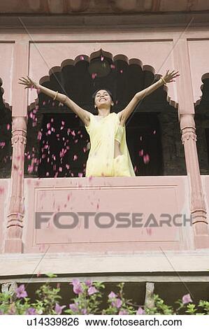 Stock Photograph - Low angle view of a young woman spreading petals from the balcony of a fort, Neemrana Fort Palace, Neemrana, Alwar, Rajasthan, India. Fotosearch