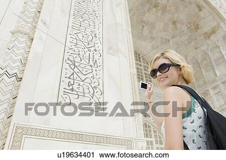 Stock Image - Low angle view of a young woman taking a picture of a mausoleum, Taj Mahal, Agra, Uttar Pradesh, India. Fotosearch