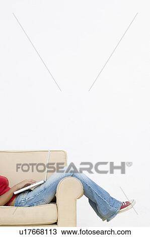 Low section view of a woman sitting in an armchair and using a laptop View Large Photo Image Stock Image - Low section view of a woman sitting in an armchair and using a laptop. Fotosearch