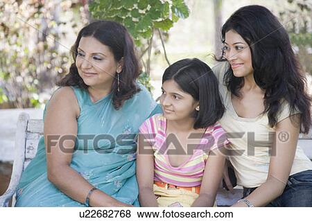 Stock Photo - Mature woman sitting on a bench with her two daughters and smiling. Fotosearch