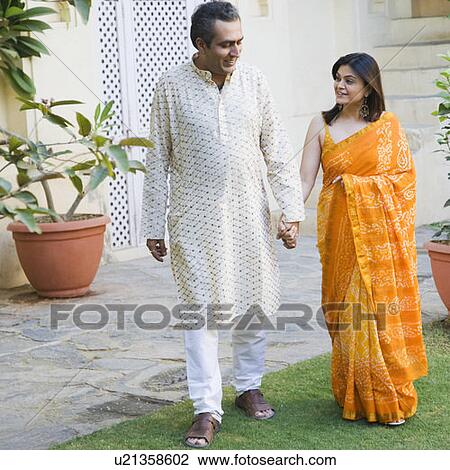 Stock Image - Mid adult couple holding hands of each other and walking. Fotosearch