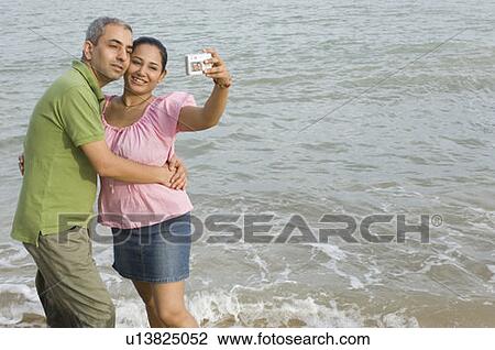 Mid adult couple taking a photograph of themselves on the beach View Large Photo Image Stock Image - Mid adult couple taking a photograph of themselves on the beach. Fotosearch