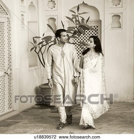 Stock Image - Mid adult couple walking with holding each other's hands. Fotosearch