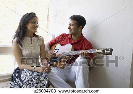 Stock Image - Mid adult man playing a guitar in front of a mid adult woman. Fotosearch