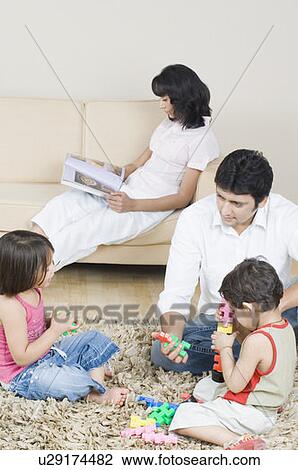 Mid adult man playing with his children and his wife reading a magazine in the background View Large Photo Image Stock Image - Mid adult man playing with his children and his wife reading a magazine in the background. Fotosearch