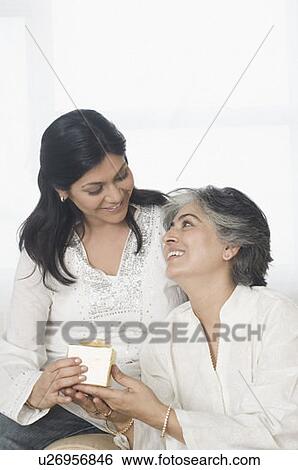 Mid adult woman giving a gift to her mother and smiling View Large Photo Image Stock Photograph - Mid adult woman giving a gift to her mother and smiling. Fotosearch