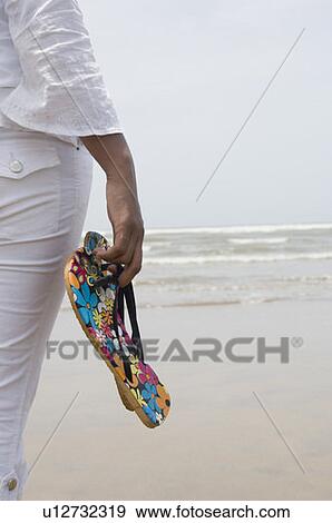 Stock Photo - Mid section view of a woman holding slippers. Fotosearch