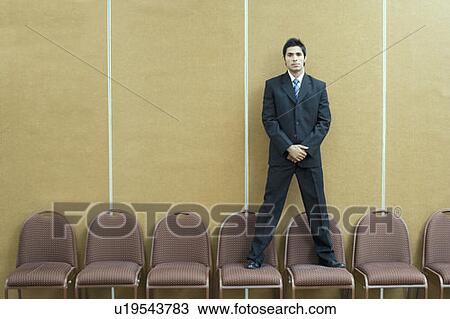 Stock Image - Portrait of a businessman standing on chairs. Fotosearch