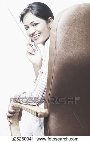 Stock Image - Portrait of a businesswoman sitting on a chair talking on a mobile phone. Fotosearch