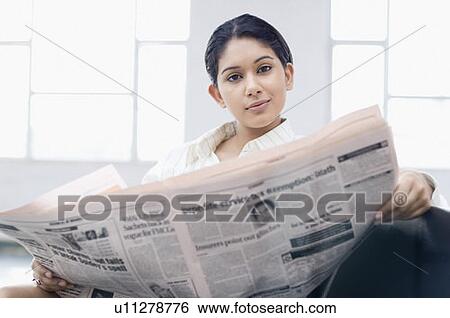 Stock Photograph - Portrait of a businesswoman sitting on a chair at an airport and reading a newspaper. Fotosearch