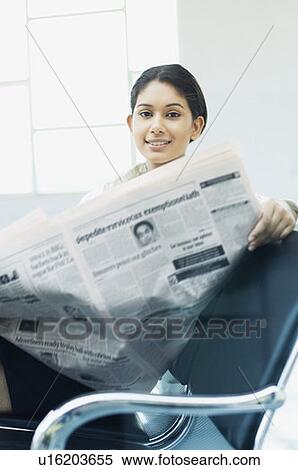 Stock Photography - Portrait of a businesswoman sitting on a chair at an airport and reading a newspaper. Fotosearch