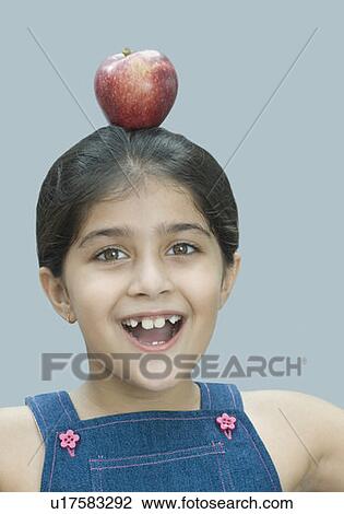 Stock Image - Portrait of a girl balancing an apple on her head. Fotosearch