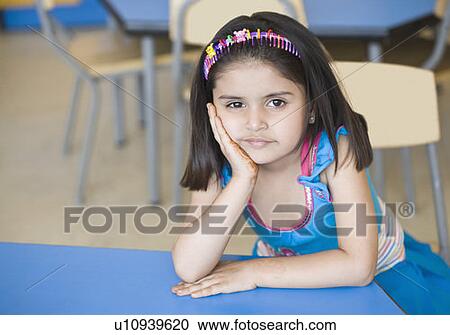 Stock Image - Portrait of a girl sitting with her hand on her chin in a classroom. Fotosearch