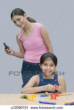 Stock Image - Portrait of a girl smiling and her mother holding a mobile phone behind her. Fotosearch