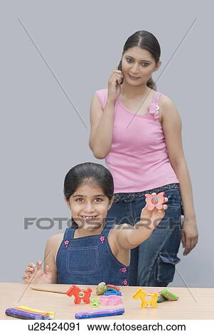 Portrait of a girl smiling and her mother talking on a mobile phone behind her View Large Photo Image Stock Image - Portrait of a girl smiling and her mother talking on a mobile phone behind her. Fotosearch
