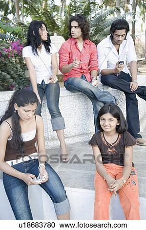 Stock Image - Portrait of a girl smiling with her friends sitting on a ledge. Fotosearch