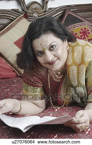Portrait of a mature woman holding a magazine lying on the bed View Large Photo Image Picture - Portrait of a mature woman holding a magazine lying on the bed. Fotosearch