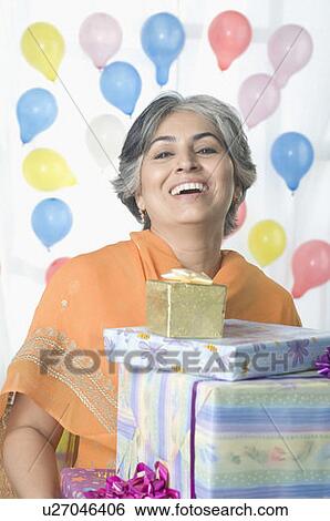Stock Photograph - Portrait of a mature woman holding birthday presents and smiling. Fotosearch