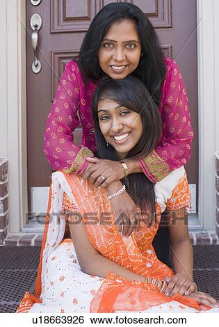Stock Photograph - Portrait of a mature woman hugging her daughter from behind and smiling. Fotosearch