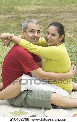Stock Photo - Portrait of a mid adult couple sitting in a park and embracing each other. Fotosearch