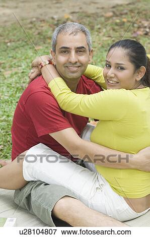 Stock Photo - Portrait of a mid adult couple sitting in a park and embracing each other. Fotosearch