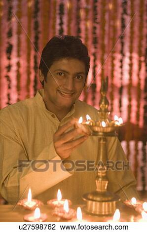 Stock Image - Portrait of a mid adult man lighting diwali lamps and smiling. Fotosearch
