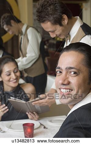 Portrait of a mid adult man smiling and a waiter taking order from a young woman in a restaurant View Large Photo Image Stock Image - Portrait of a mid adult man smiling and a waiter taking order from a young woman in a restaurant. Fotosearch