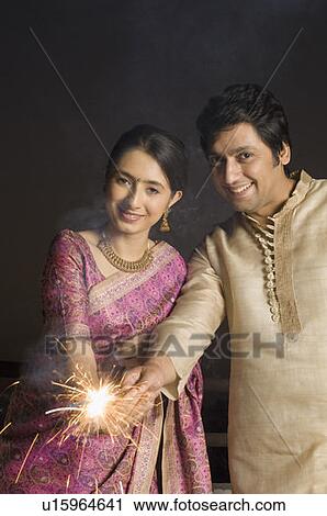 Stock Image - Portrait of a mid adult man with a young woman burning firecrackers. Fotosearch