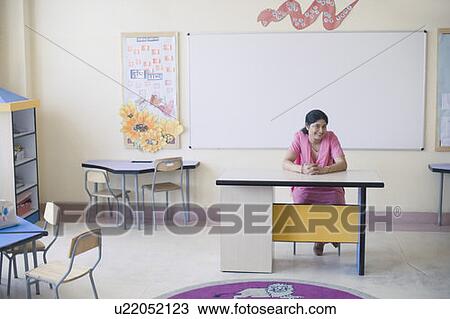 Portrait of a mid adult woman sitting at a desk and smiling in a classroom View Large Photo Image Stock Image - Portrait of a mid adult woman sitting at a desk and smiling in a classroom. Fotosearch