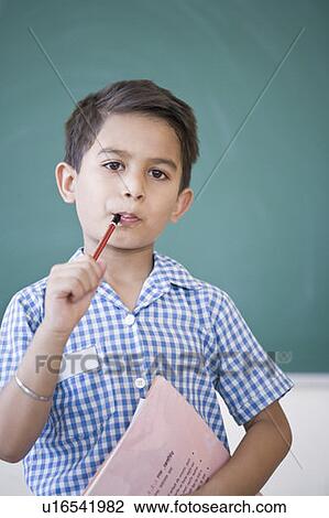 Portrait of a schoolboy holding a pencil and a book in front of a blackboard View Large Photo Image Stock Image - Portrait of a schoolboy holding a pencil and a book in front of a blackboard. Fotosearch
